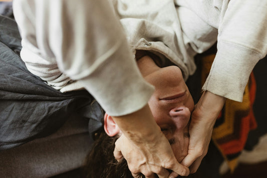 A man laying off the edge of his bed upside down looking stressed, head in his hands