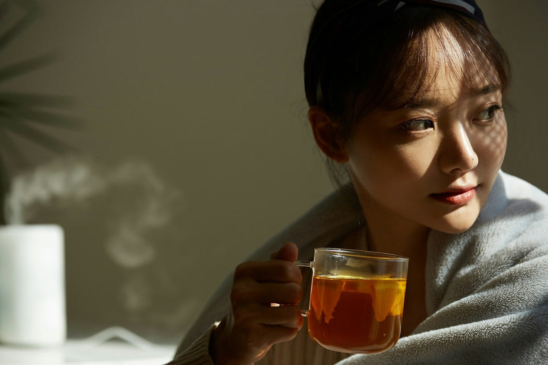 An Asian lady drinking tea in bed, a diffuser running in the background