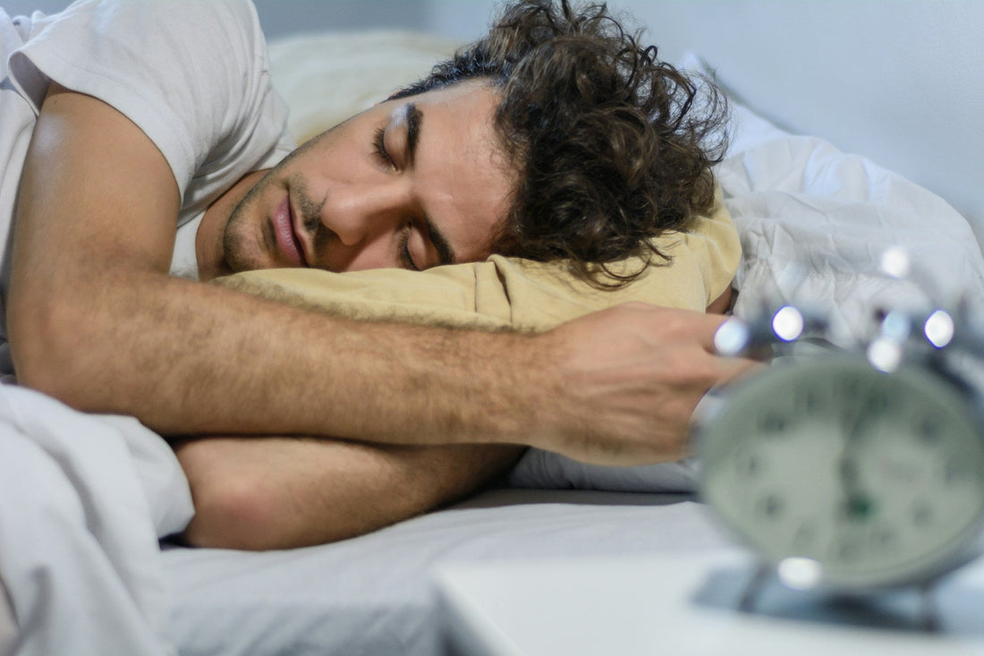 A man sleeps with his alarm clock on the bedside table